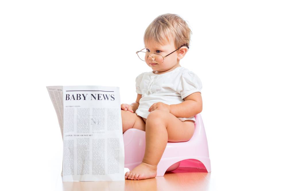 niña pequeña sentada en una bacinilla y leyendo el periódico