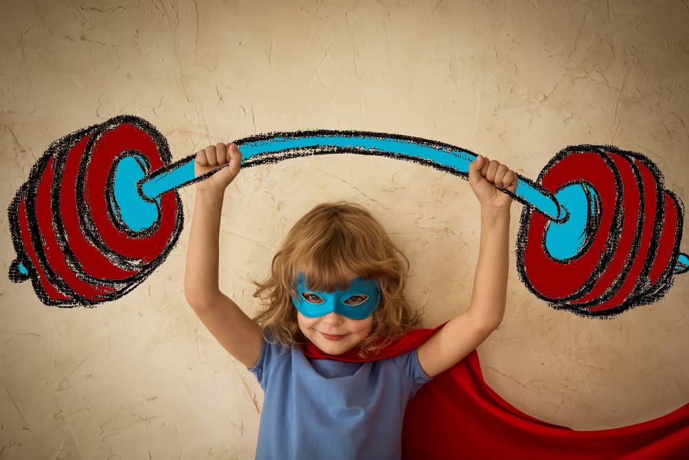 niña pequeña vestida de superhéroe levantando pesas imaginarias