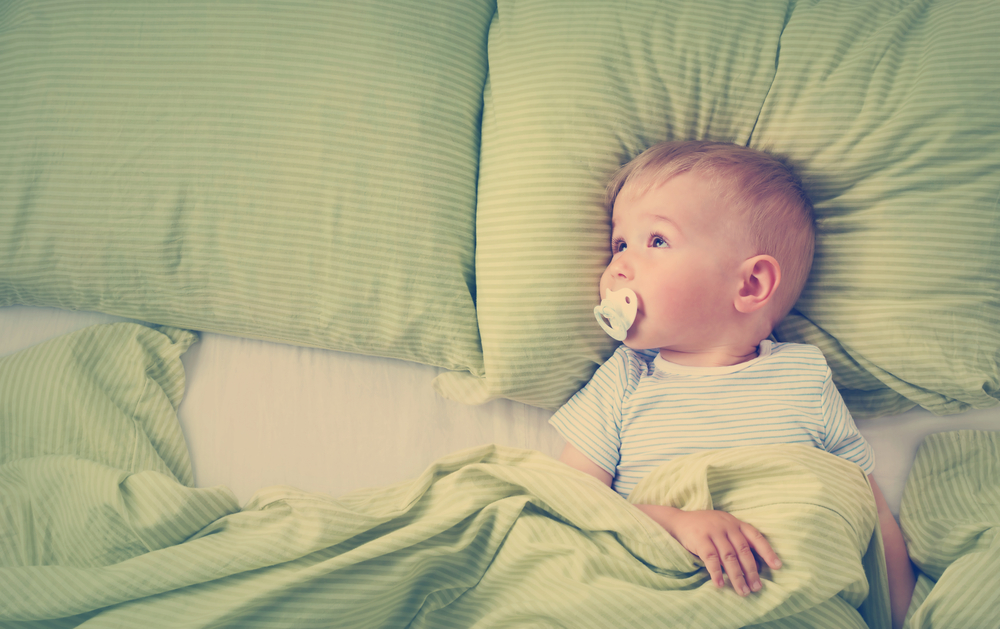 niño pequeño con chupón acostado en su cama