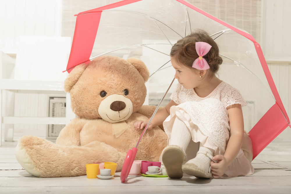 niña pequeña sentada bajo un paraguas con su oso de peluche