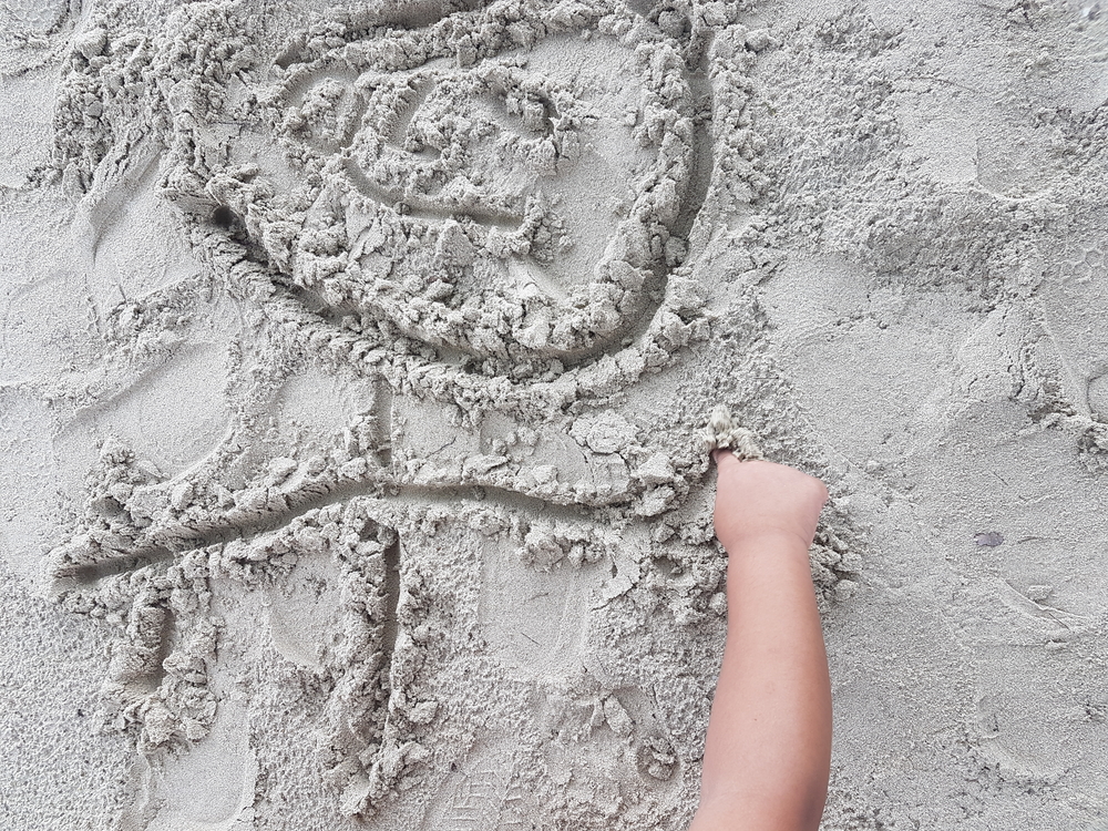niño pequeño dibujando en la arena