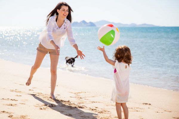 niña lanzándole una pelota a su mamá en la playa