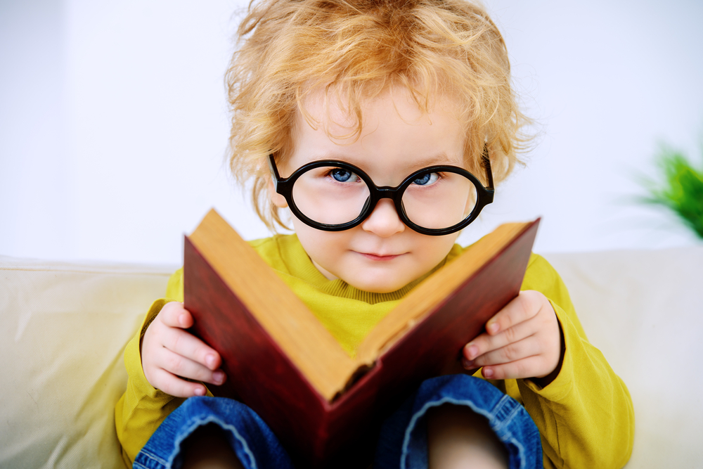niño pequeño con lentes leyendo un libro para niños de preescolar