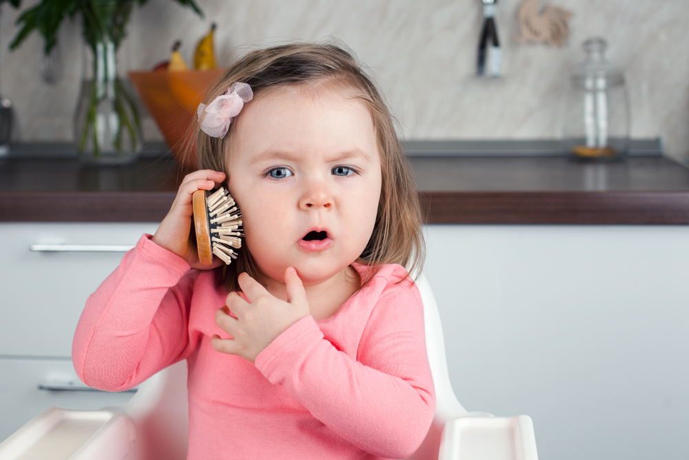 desarrollo del lenguaje: bebita sosteniendo un cepillo como si fuera un teléfono