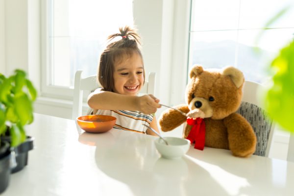 niña pequeña dándole de comer a su oso de peluche