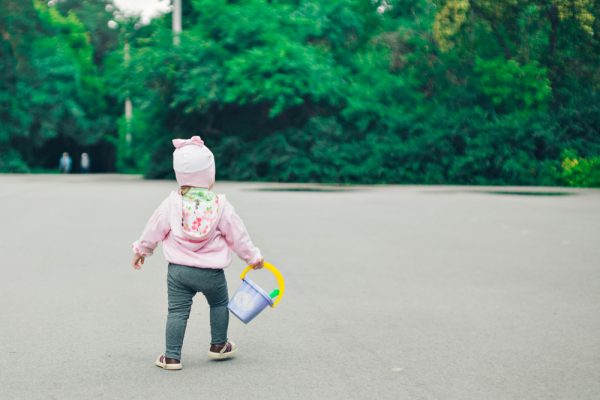 niña pequeña caminando sosteniendo una cubeta de plástico