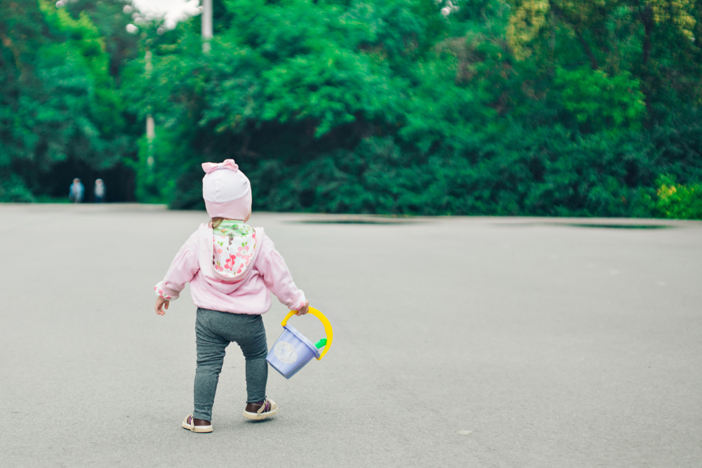 niña pequeña caminando sosteniendo una cubeta de plástico