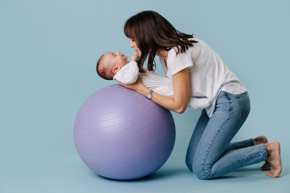 mamá apoyando a su bebé sobre una pelota de yoga