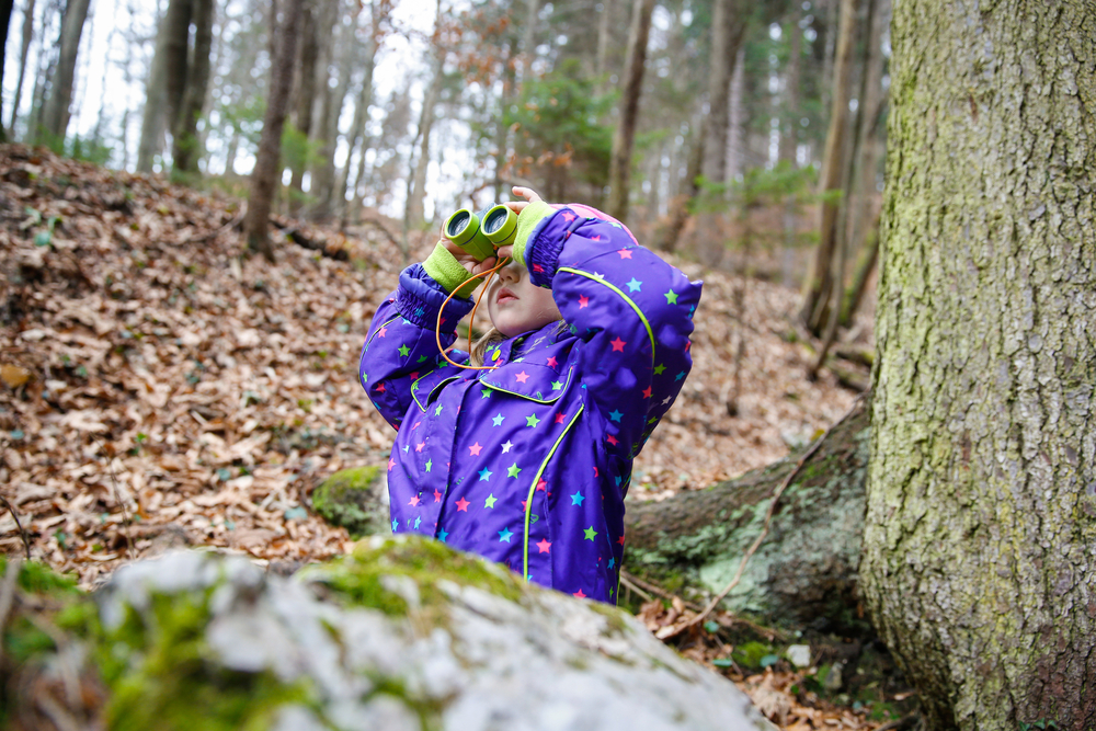 niña pequeña usando binoculares en un bosque